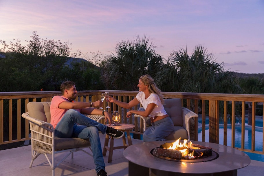 Twee mensen proosten op een terras met zwembad op de achtergrond